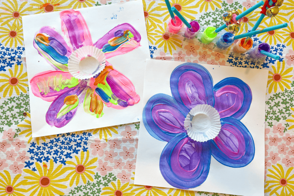 Two finished cupcake Liner Flower Art  pieces (white paper with a white cupcake liners glued to the middle and colorful petals painted around the cupcake liner centers). 