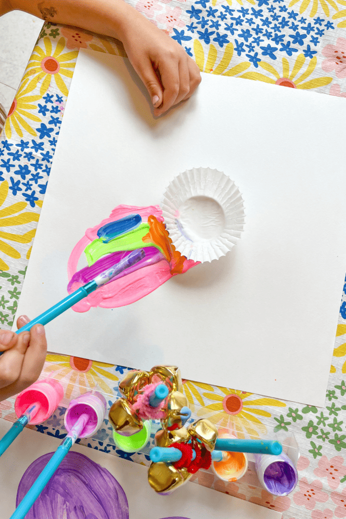 A child paints a flower petal on her Cupcake Liner Flower Art (a white paper with a white cupcake liner glued to the middle and colorful petals painted around the cupcake liner center). 