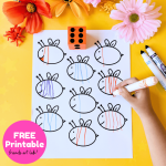 A paper worksheet for the preschool bee math activity with nine bee outlines sits on a yellow table surrounded by plastic insects and faux flowers. An orange die sits with six dots facing up, and a young child's hand draws orange stripes on one of the bees.