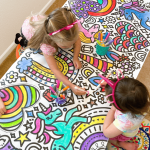 Two preschool kids use markers to color in the giant rainbows & unicorns coloring banner