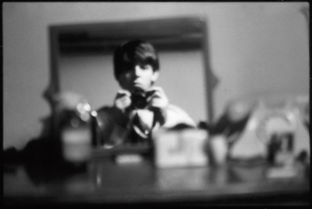 A blurry photograph of a white man pointing a camera at himself in a mirror.